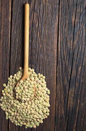 Raw green lentils in spoon on dark wooden surface, top view. Space for textの写真素材