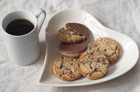 Plate in the shape of heart with chocolate cookies and black coffee for breakfast
