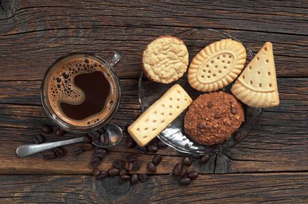 Different shortbread cookies and cup of hot coffee on old wooden background, top view