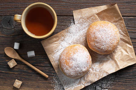 Doughnuts with powdered sugar and cup of tea on a dark wooden background, top view