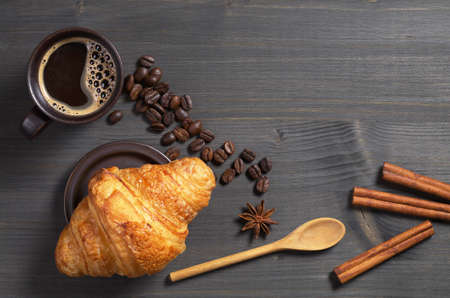 Cup of hot coffee and fresh croissant on dark wooden table, top viewの写真素材