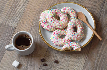 Cup of coffee and sugar cookies with sprinkles in plate on tableの写真素材