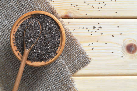 Chia seeds in bowl and spoon on a burlap on the wooden table, top viewの写真素材
