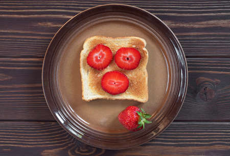Toasted bread with strawberries in plate on dark wooden table, top view