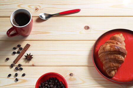 Cup of hot coffee and fresh croissant for breakfast on wooden table. Red tableware の写真素材