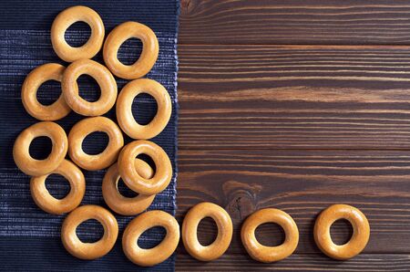 Small dry bagels on dark wooden table with blue napkin, top view. Space for text