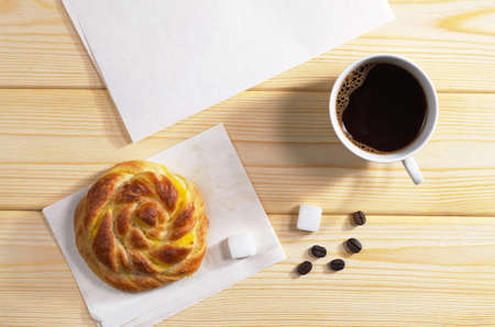 Cup of hot coffee and sweet bun for breakfast on wooden background, top view