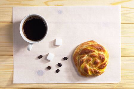Cup of black coffee and fresh bun for breakfast on wooden table, top viewの写真素材