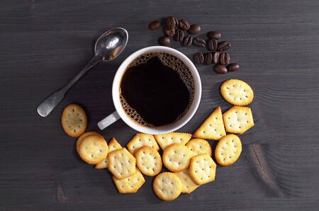 Cup of hot coffee and crackers with cheese flavor on dark wooden table, top viewの写真素材