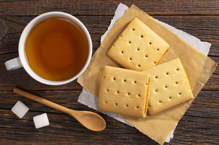 Cup of tea and square cookies with jam for breakfast on old wooden table, top viewの写真素材