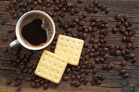 Cup of hot coffee and square crackers on dark wooden table, top viewの写真素材