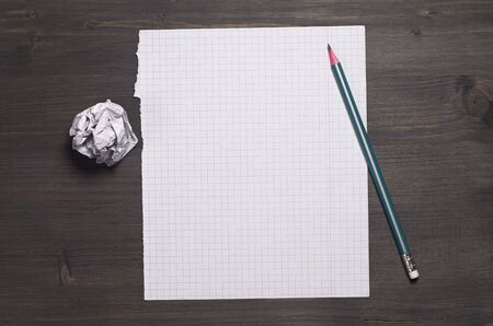 Empty sheet from school notebook, crumpled paper and pencil on dark wooden desk, top view. Space for textの写真素材