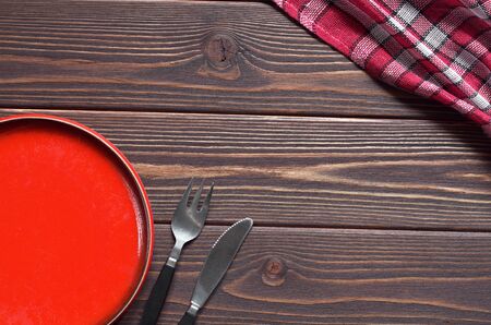 Empty red plate and cutlery on brown wooden table, top view. Space for text