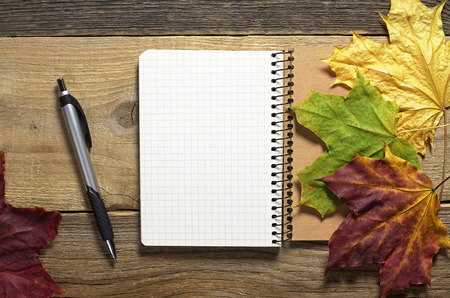 Opened notepad with a pen and maple leaves on old wooden background, top view. Autumn conceptの写真素材