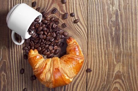 Croissant and cup with coffee beans on wooden background, top view. Space for your textの写真素材