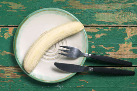 Banana in plate and cutlery on old green wooden table, top viewの写真素材