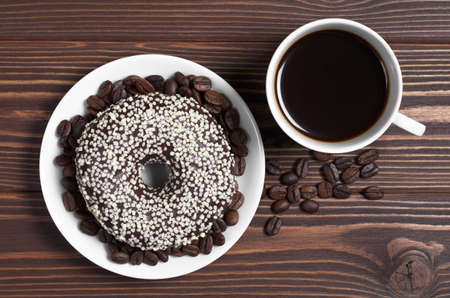 Cup of hot coffee and delicious donut decorated with white chocolate on brown wooden table, top view