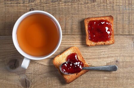 Cup of tea and small toast bread with jam on old wooden table, top view