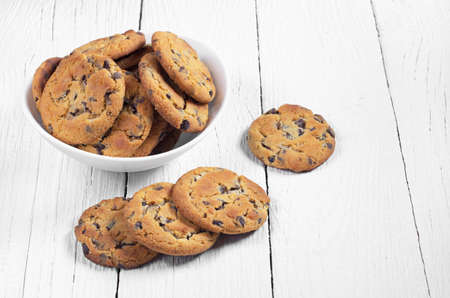 Cookies with chocolate chips in bowl and near on the white wooden table with cope space