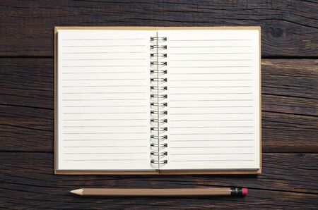 Notepad in hardcover with a pencil on dark wooden background, top view. Space for your textの写真素材