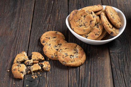 Chocolate chip cookies in bowl and crumbs on dark wooden background