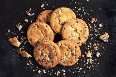 Pile of chocolate chip cookies and crumbs on an old black metal background, top view 