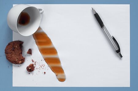 Coffee spilled on the paper with chocolate cookie and pen on blue desk. Conceptual photo 