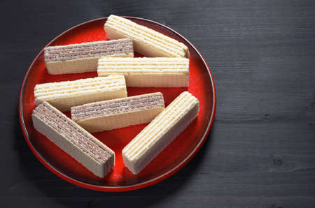 Wafers with chocolate and vanilla in red plate on black wooden backgroundの写真素材