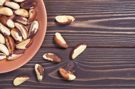 Brazil nuts in plate and scattered on brown wooden table, top view with space for textの写真素材