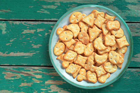 Small salty crackers of different shapes in plate on old green wooden background, top view with space for textの写真素材