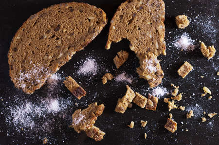 Pieces of bread with salt on old black metal as a background of food, top view, contrast low lightの写真素材