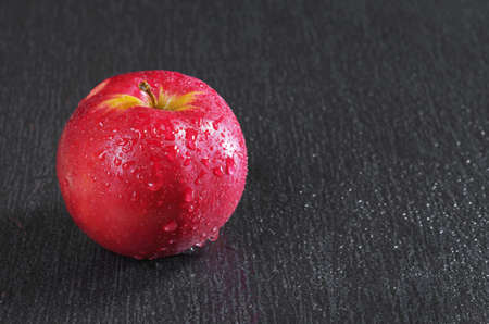 Red apple close-up with water drops on a black stone background with space for textの写真素材