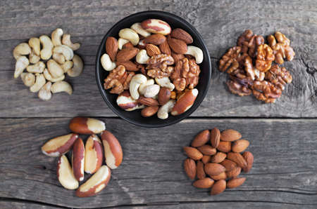 Mixed nuts in black bowl and on old wooden table, top view. Selective focus