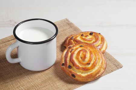 Buns with raisins and enameled mug of milk on a light wooden tableの写真素材
