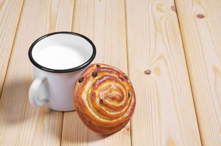 Bun with raisins and enameled mug of milk on the wooden tableの写真素材