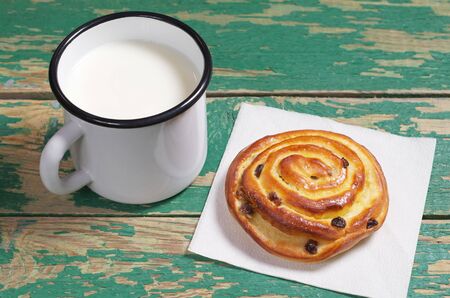 Mug of milk and bun with raisins on old green wooden table close-upの写真素材