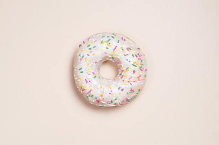Donut with glaze decorated with colorful sprinkles on a light brown background, top view