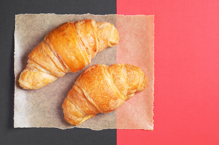 Two fresh croissants on paper is located on black and red background, top viewの写真素材