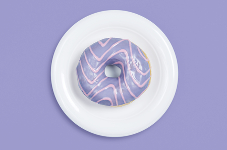 Donut with colored glaze in white plate on violet background, top viewの写真素材