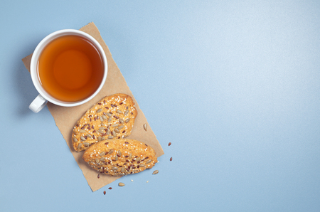 Cup of tea and oatmeal cookies with sunflower and flaxseeds on blue table, top view with copy spaceの写真素材