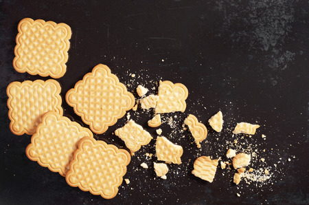 Whole and broken vanilla square cookies on old black metal background, top viewの写真素材