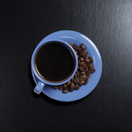 Blue cup of coffee and beans is located in the center of a black stone background, top viewの写真素材