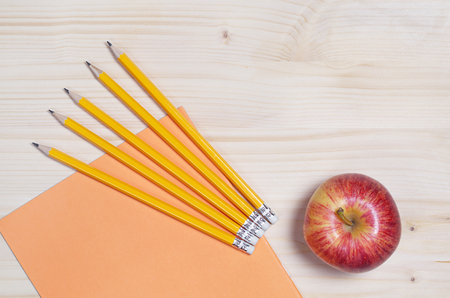 School notebook, pencils and red apple on the light wooden desk. Top view with space for text. Education conceptの写真素材