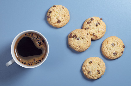 Top view of a cup of coffee and biscuits with chocolate on a blue tableの写真素材