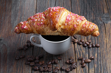 Raspberry croissant on a cup of coffee is located on an old wooden tableの写真素材