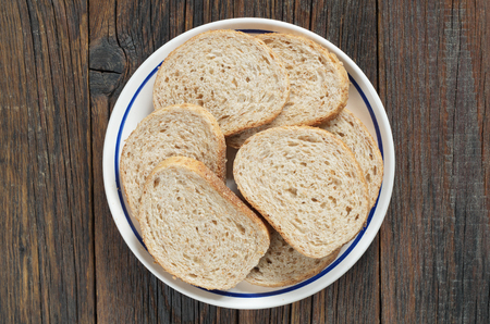 Slices of wheat bread with bran in a plate on old wooden background, top viewの写真素材