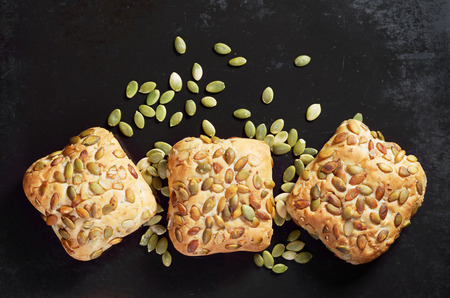 Buns with pumpkin seeds on old black metal background, top view