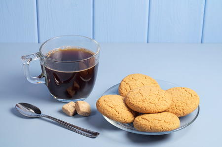 Oatmeal cookies and cup of hot coffee in transparent dishes on blue table