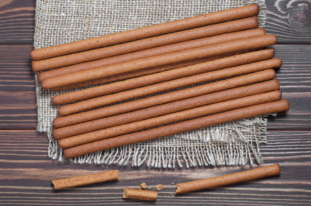 Heap of rye bread sticks on burlap is located on brown wooden background, top view
