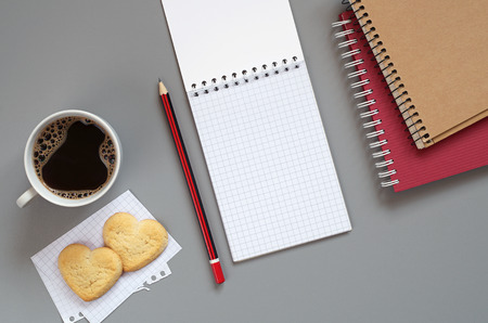 Notebook, pencil and cup of coffee with cookies in the shape of a hearton gray desk, top view